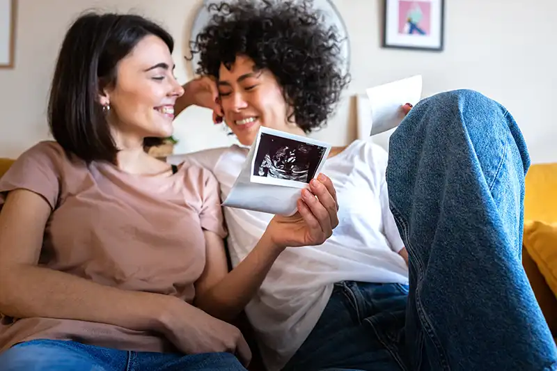 Sonriente pareja embarazada de lesbianas/LGBTQ+ mirando una ecografía