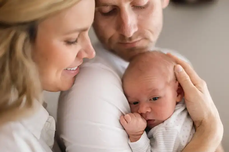 Blonde, first-time mother smiles as she helps first-time father hold new baby after having INVOcell