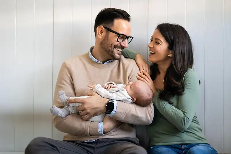 Una joven pareja sonriente sosteniendo a su nuevo bebé después de elegir la reproducción por parte de terceros