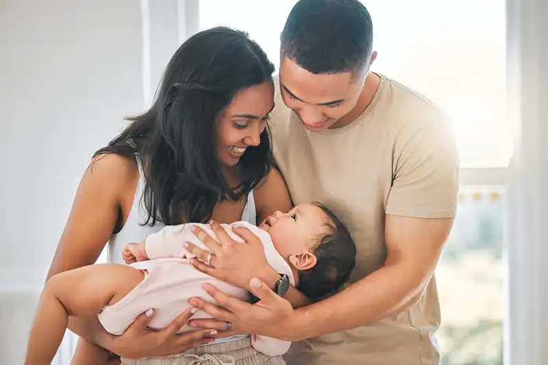Feliz pareja de jóvenes negros sosteniendo a su nuevo bebé y sonriendo después de aprender las claves para una IIU exitosa