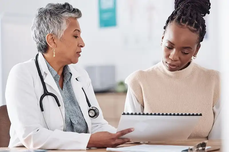 Young Black woman and female doctor discuss her infertility testing results at fertility clinic.