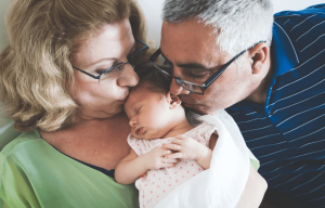 Older man and woman kissing a newborn baby's cheeks